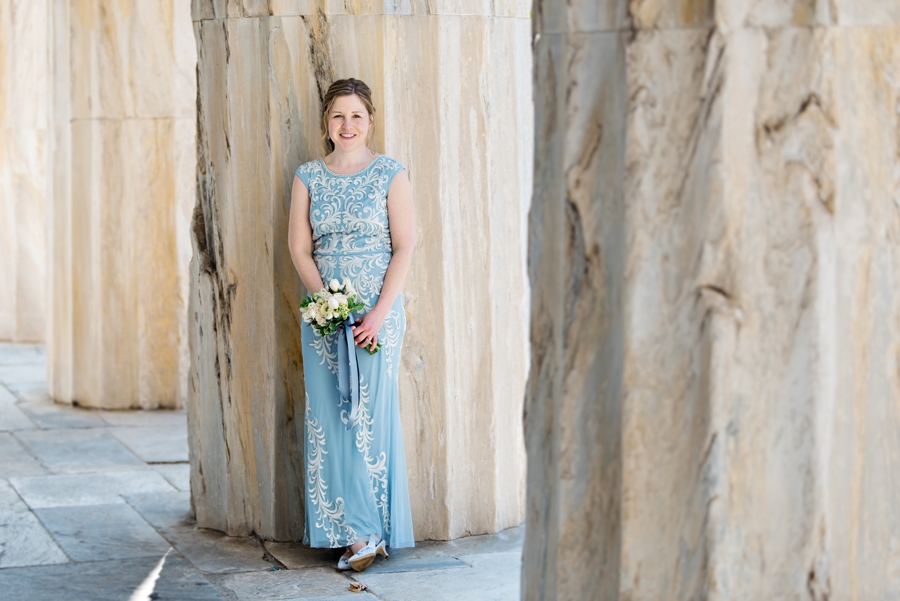 A beautiful bride in a blue and white wedding dress leaning against a column in Old City Philadelphia.